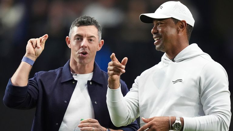 Rory McIlroy and Tiger Woods stand on the green as they watch New York Golf Club and The Bay Golf Club warmup for the inaugural match of the TMRW Golf League, Tuesday, Jan. 7, 2025, in Palm Beach Gardens, Fla. TGL features six teams of four players competing against each other in a tech-infused arena the size of a football field. (AP Photo/Rebecca Blackwell)