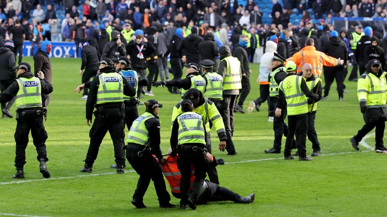 An injured steward is helped by police officers as fans invade the pitch at Ibrox